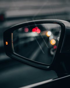A close-up of a car's side mirror reflecting bokeh lights on a night drive.
