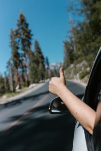 Hand giving thumbs up from car window on a scenic road trip through nature.